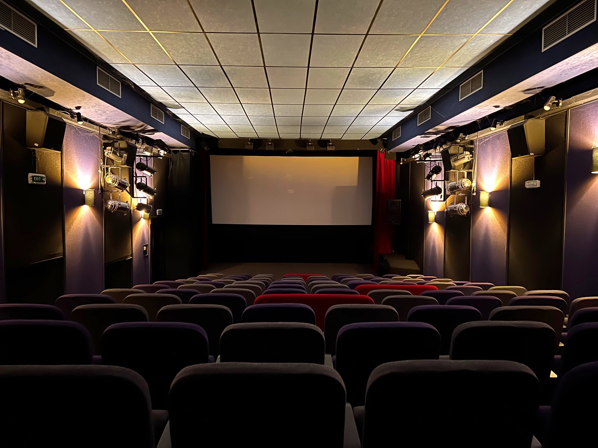Kinosál se svažujícími se řadami sedaček a vepředu promítací plátno.