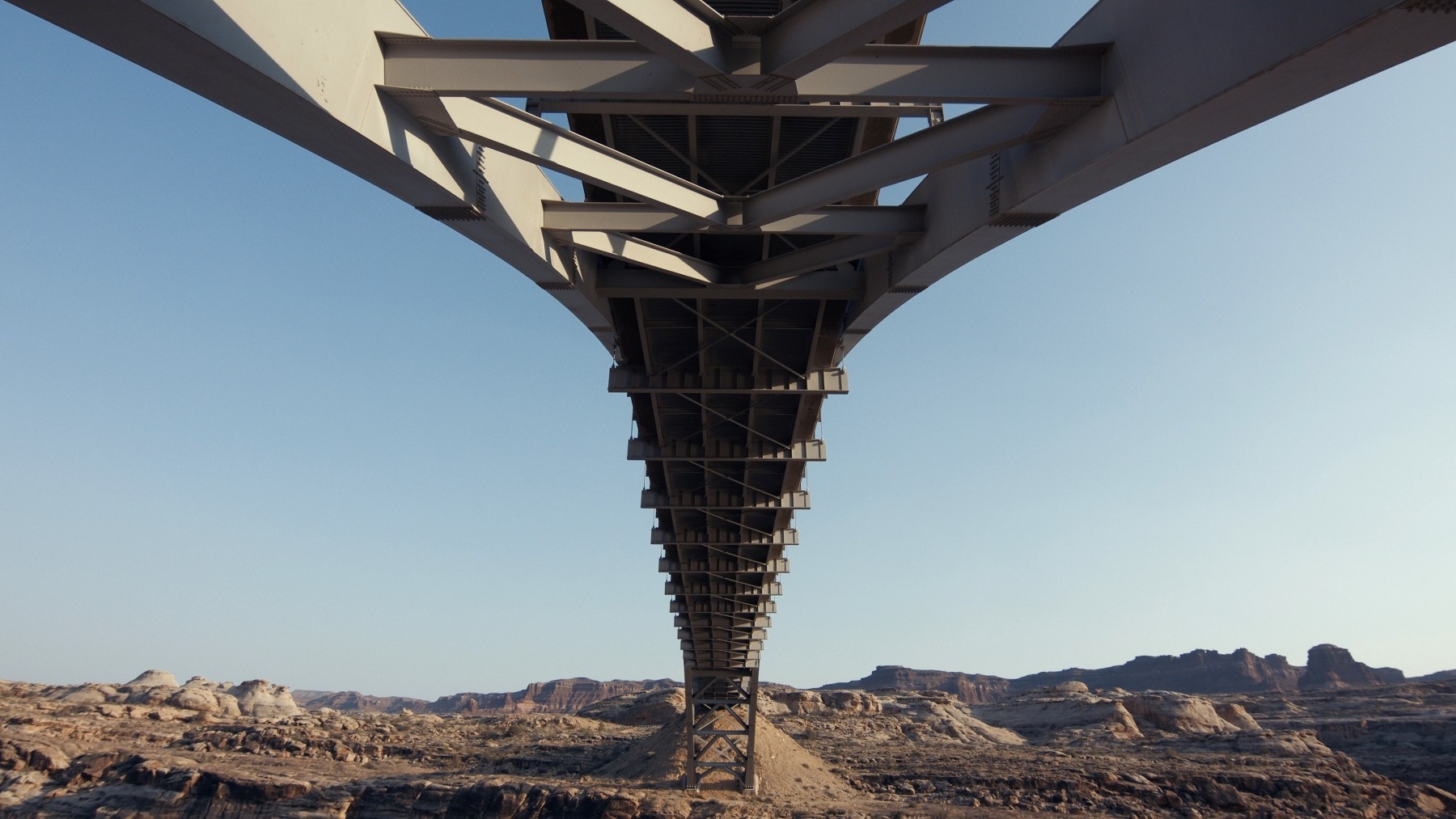 Kovový most focený ze spodu. Vzadu jde vidět vyschlá krajina s horami.