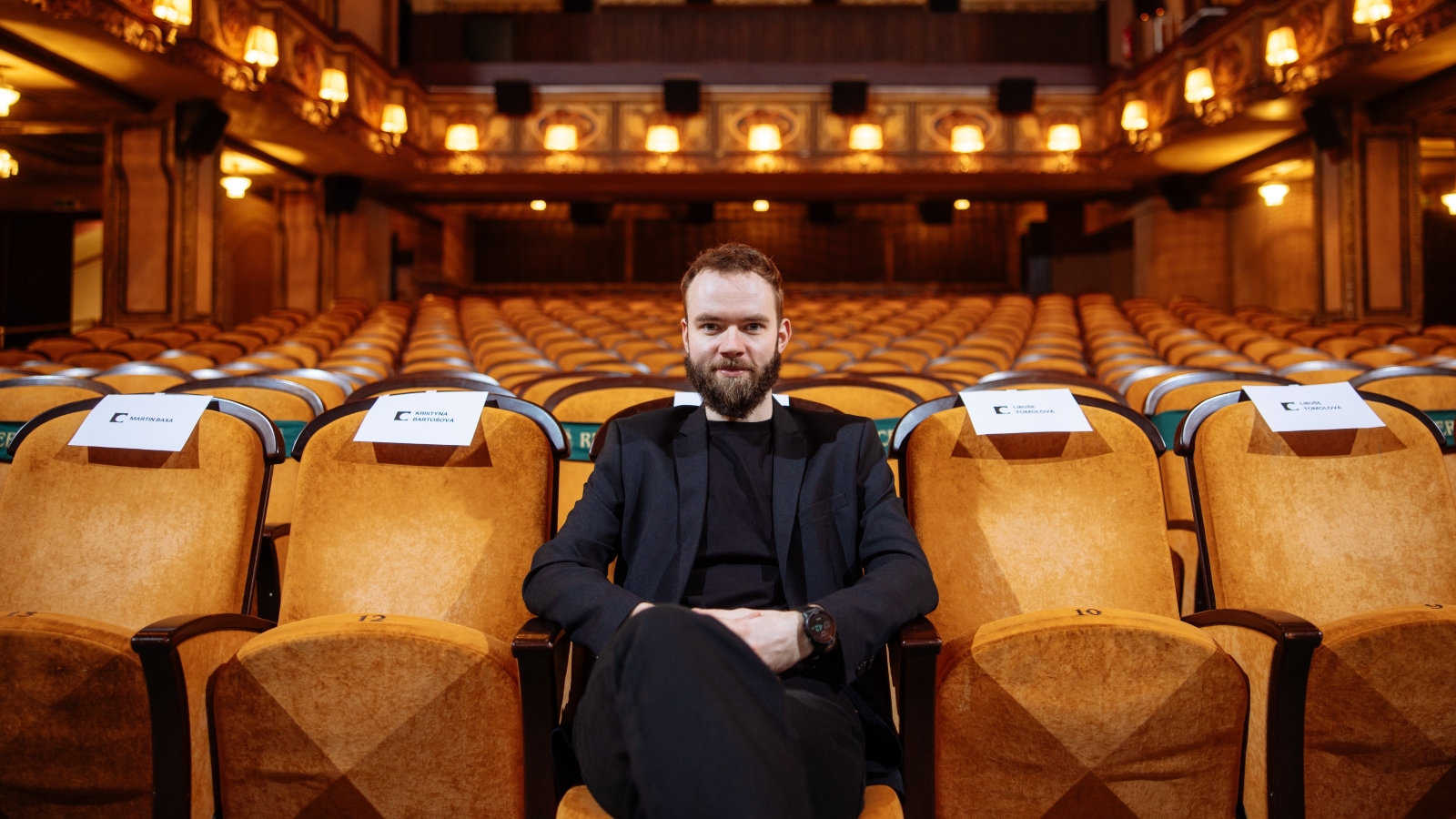 Muž sedí na sedadle uprostřed první řady prázdného kinosálu.