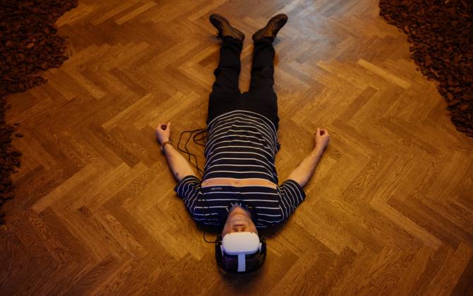 Muž leží na zemi s roztaženýma rukama a má nasazené brýle pro sledování virtuální reality.