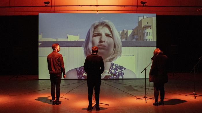 Zažijte něco víc Tři lidé stojí před plátnem, na kterém je hlava ženy.