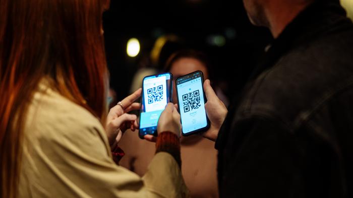 Zůstaňte v obraze Dva lidé stojí vedle sebe a drží v rukou mobilní telefony s otevřenými obrazovkami, na kterých je zobrazen stejný QR kód.