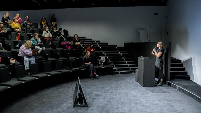 HR benefity Žena mluví do mikrofonu a přednáší publiku.