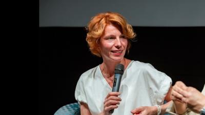 Sedící žena hovoří do mikrofonu.